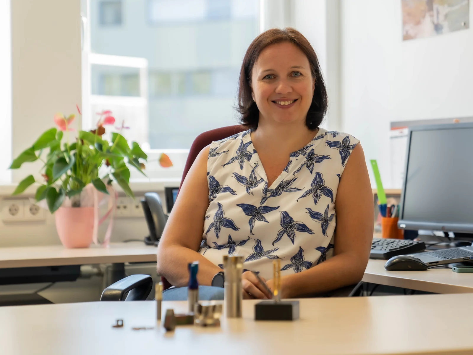 Nina Schalk sitzt in ihrem Büro und lächelt in die Kamera, wärend auf ihrem Schreibtisch verschiedene Schneidewerkzeuge liegen