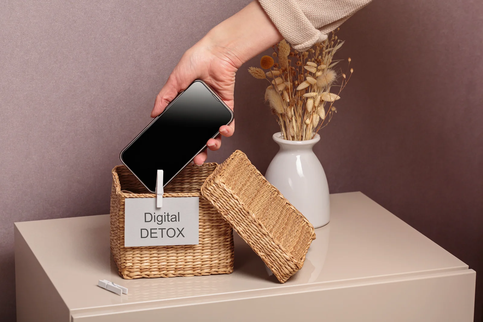 Eine junge Dame legt ihr Smatphone in eine Box, welche die Aufschrift "Digital Detox" trägt.